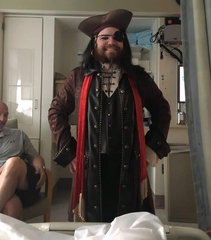 Costumed man dressed as a pirate with eye patch, hat, and pirate attire smiling.