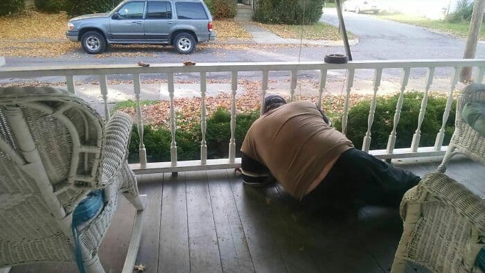 Man leaning over porch railing, looking down, in a humorous pose.