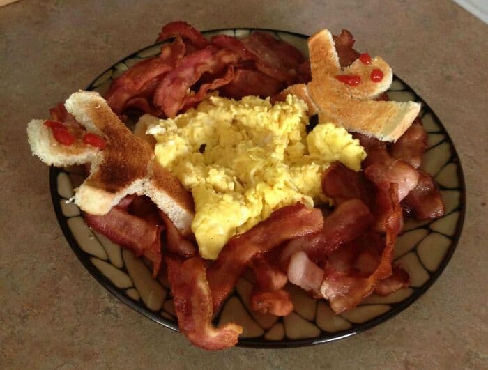 Plate of scrambled eggs, crispy bacon, and toast with ketchup.