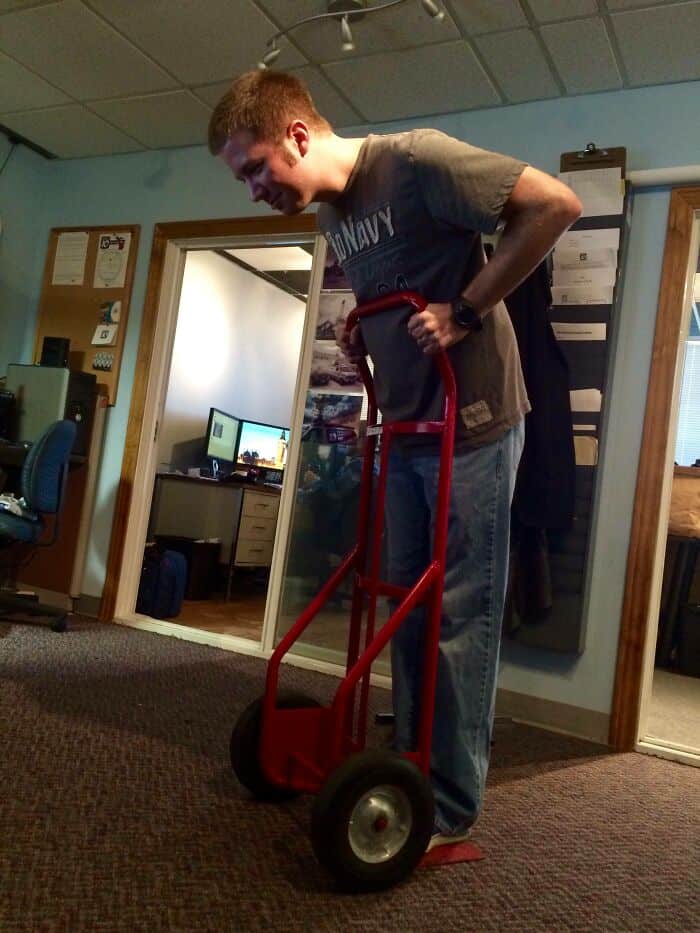 Wholesome man smiling with a red hand truck in an office setting.