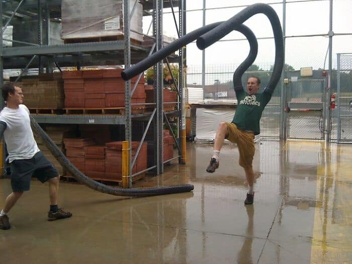 Two men playfully interacting with large industrial vacuum hoses outside.