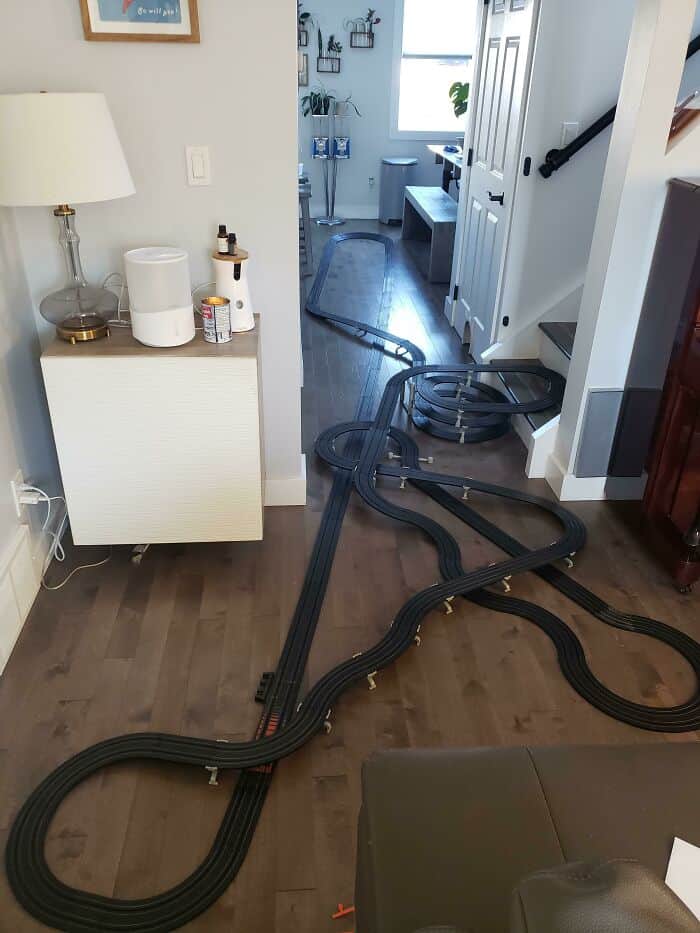 Funny men wholesome scene with a toy train track running through a living room.