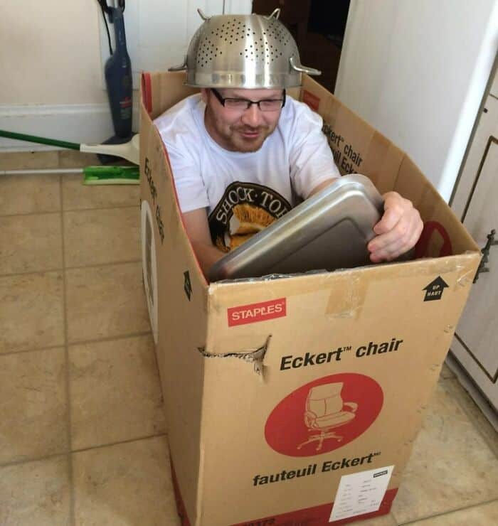 Man in a cardboard box with a colander helmet, showcasing a humorous and wholesome moment.