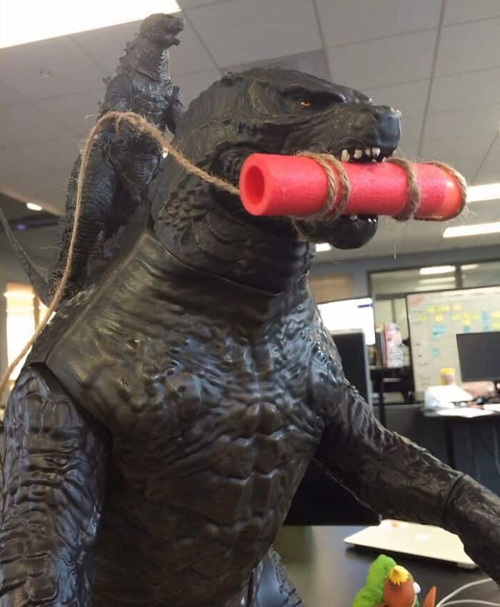 Godzilla costume with a firecracker in its mouth, humorous office scene.