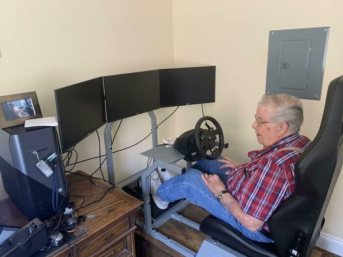 Elderly man enjoying a driving simulation with multiple monitors and steering wheel.