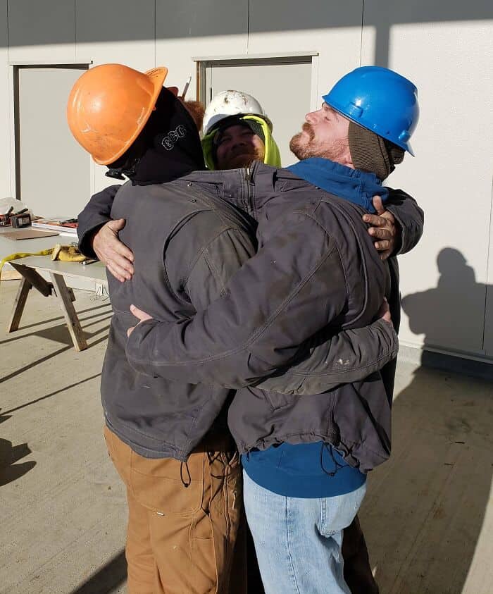 Men in safety helmets sharing a joyful embrace, celebrating teamwork and camaraderie.
