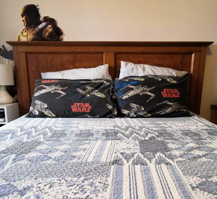 Star Wars themed pillowcases on a bed with a wooden headboard.
