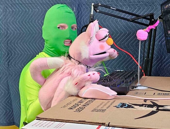Man in green ski mask with pig puppet at DJ booth, humorous and playful scene.