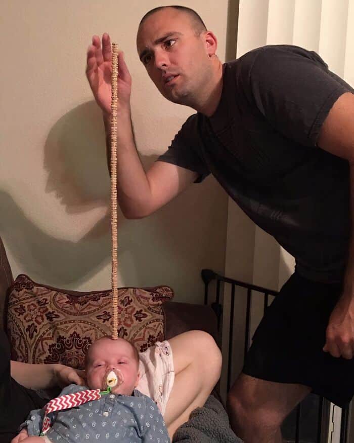 Wholesome man holding a long string of pasta near a sleeping baby with pacifier.