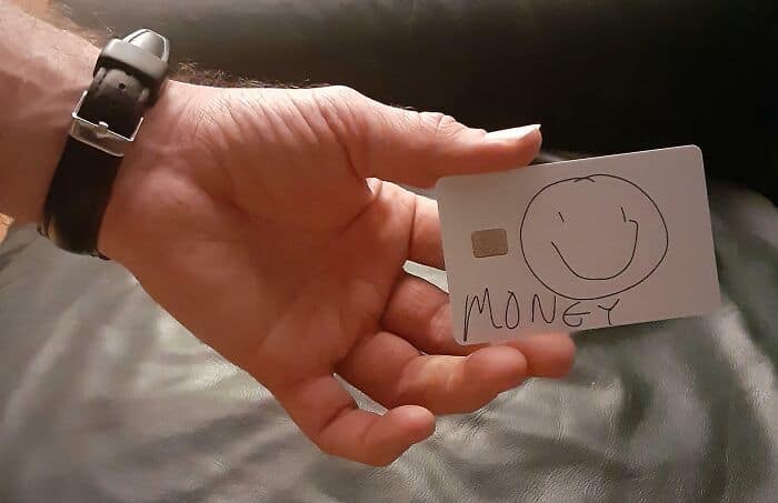 Hand holding a card with a smiley face and the word "MONEY" written on it.