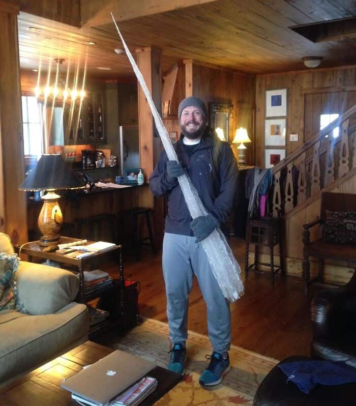 Man smiling with oversized sword in warm, rustic home setting.
