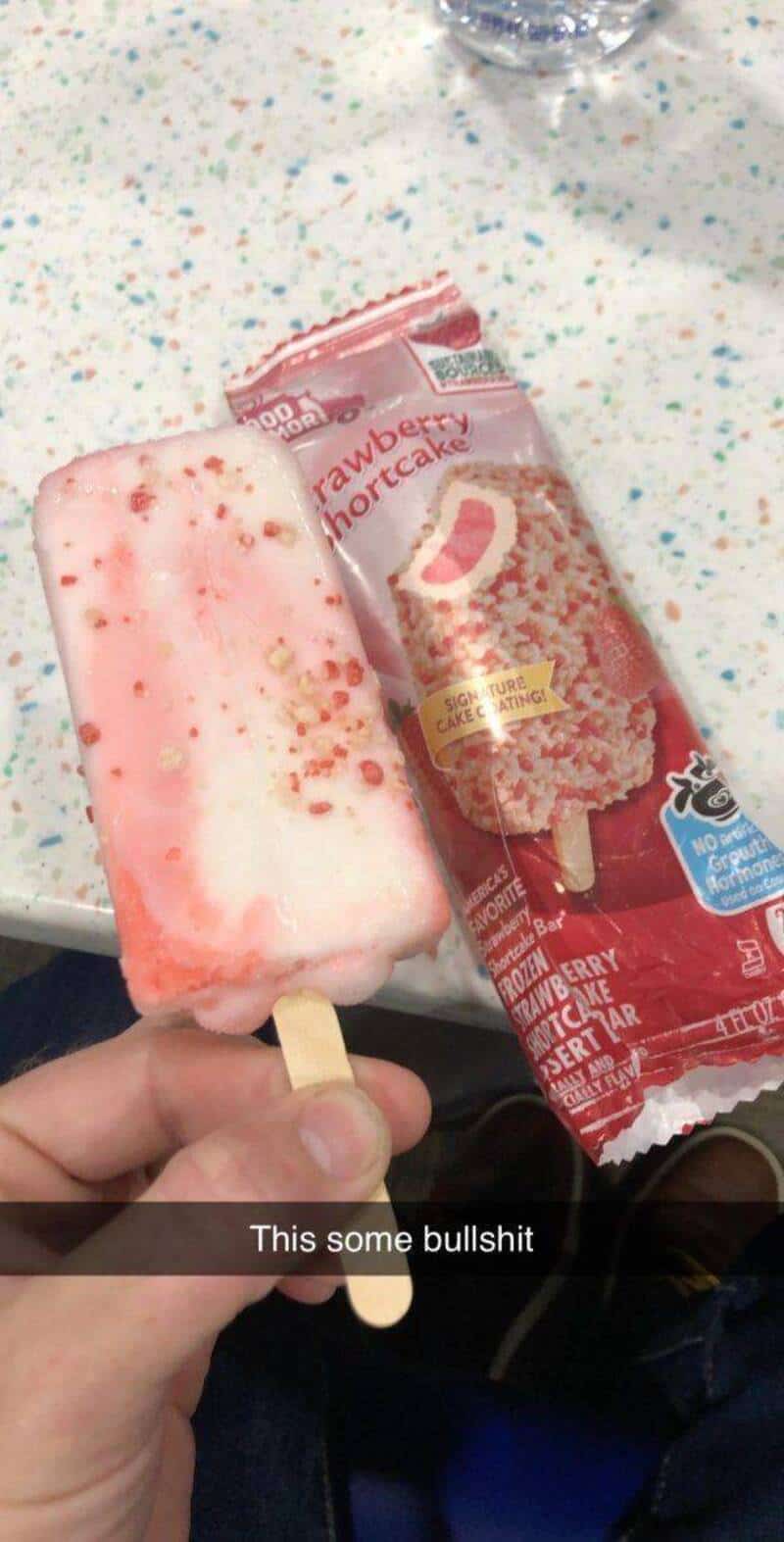 Hand holding a strawberry shortcake ice cream bar with packaging nearby.
