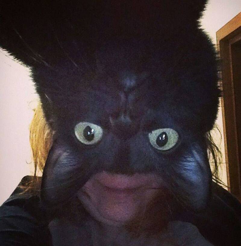 Upside-down black cat with large eyes and humorous face.