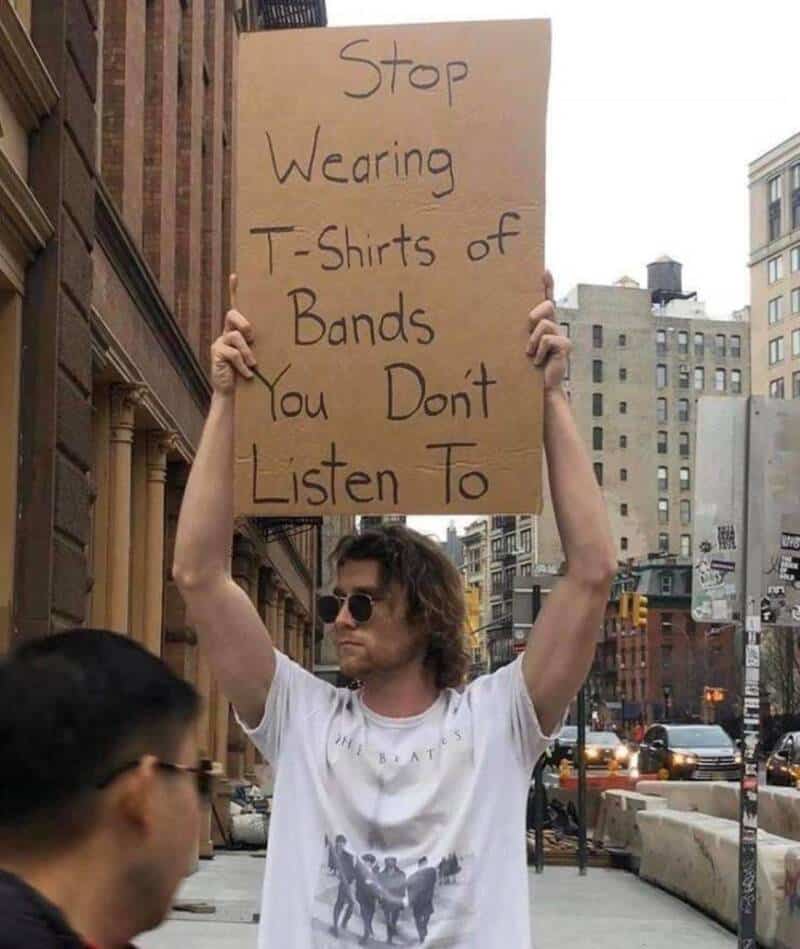 Person holding a sign that says "Stop Wearing T-Shirts of Bands You Don't Listen To".