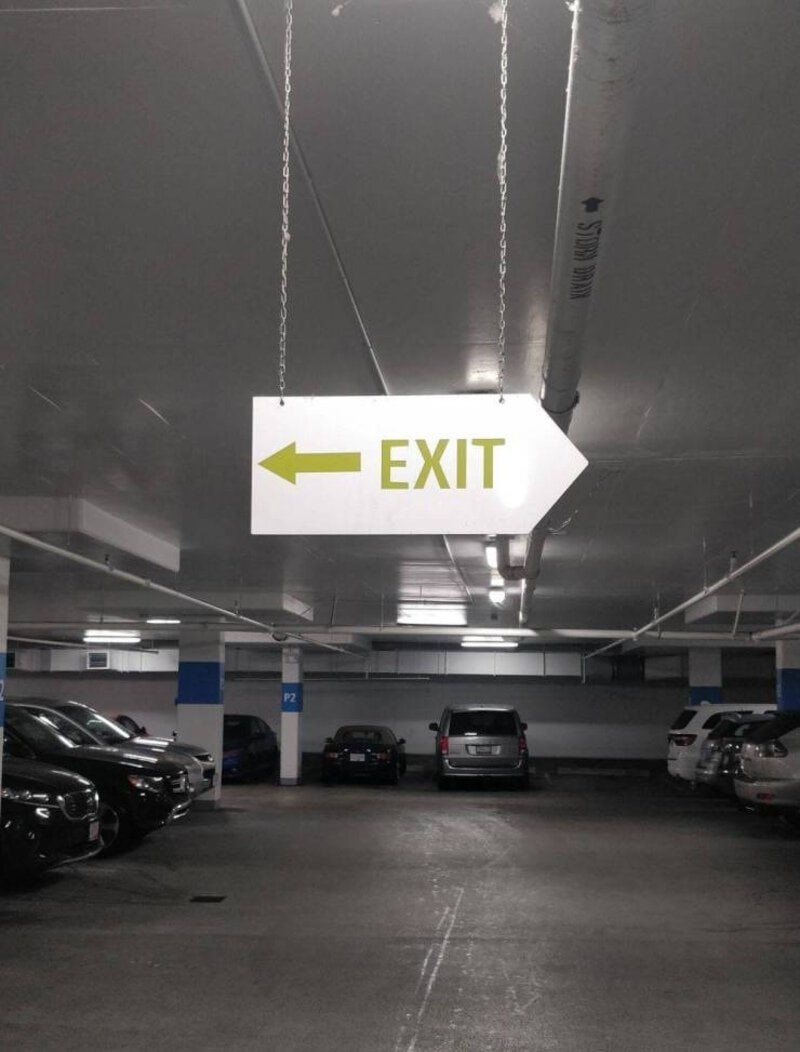 Exit sign in underground parking lot indicating direction to the exit.