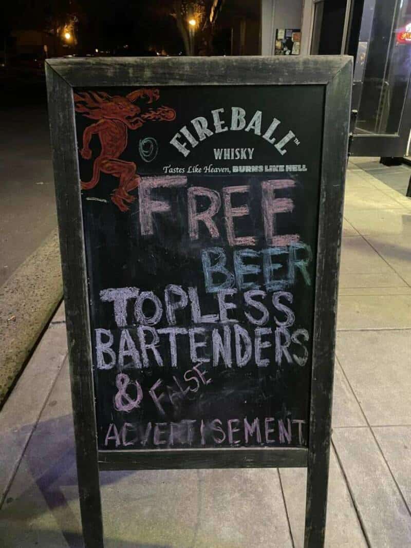 Chalkboard sign advertising free top-shelf bartenders and false advertising at a bar.