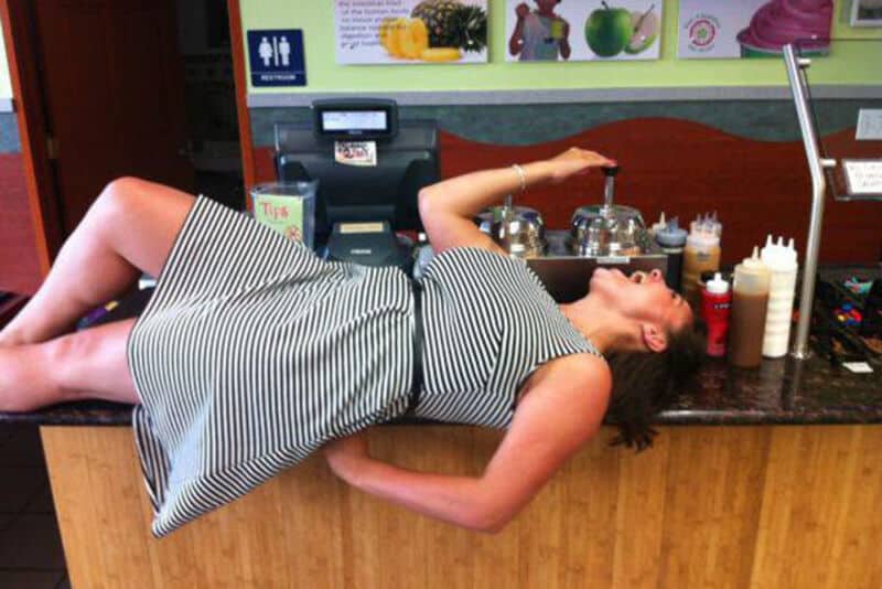 Woman relaxing on a restaurant counter with kitchen tools and condiments in the background.