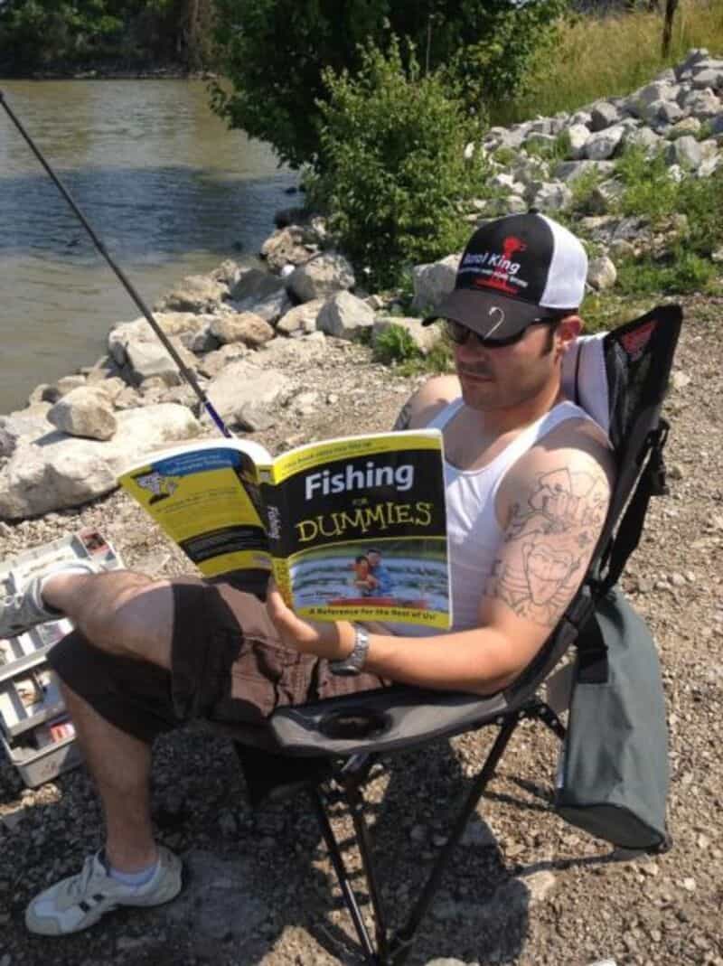 Fishing man relaxing outdoors with a book near water.