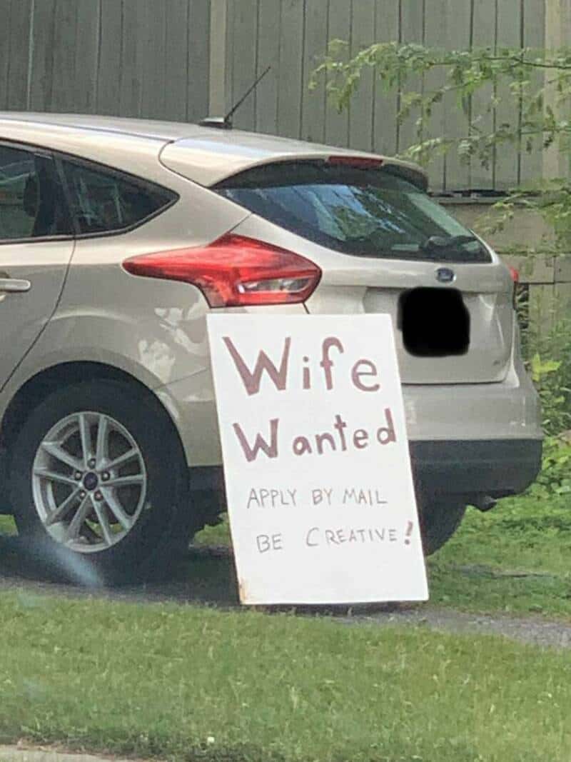 Car with a humorous "Wife Wanted" sign on the back, promoting creativity in marriage ads.
