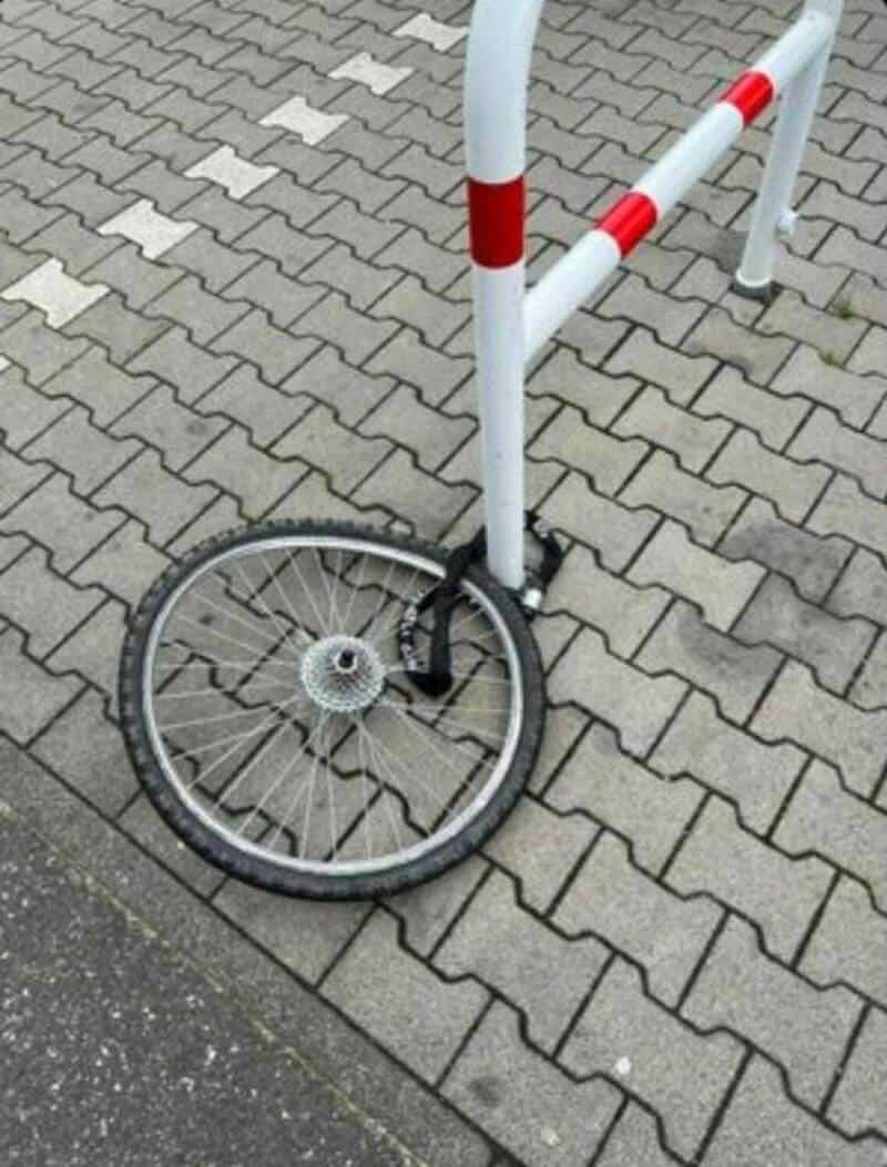 Damaged bicycle wheel locked to bike rack on paved sidewalk.