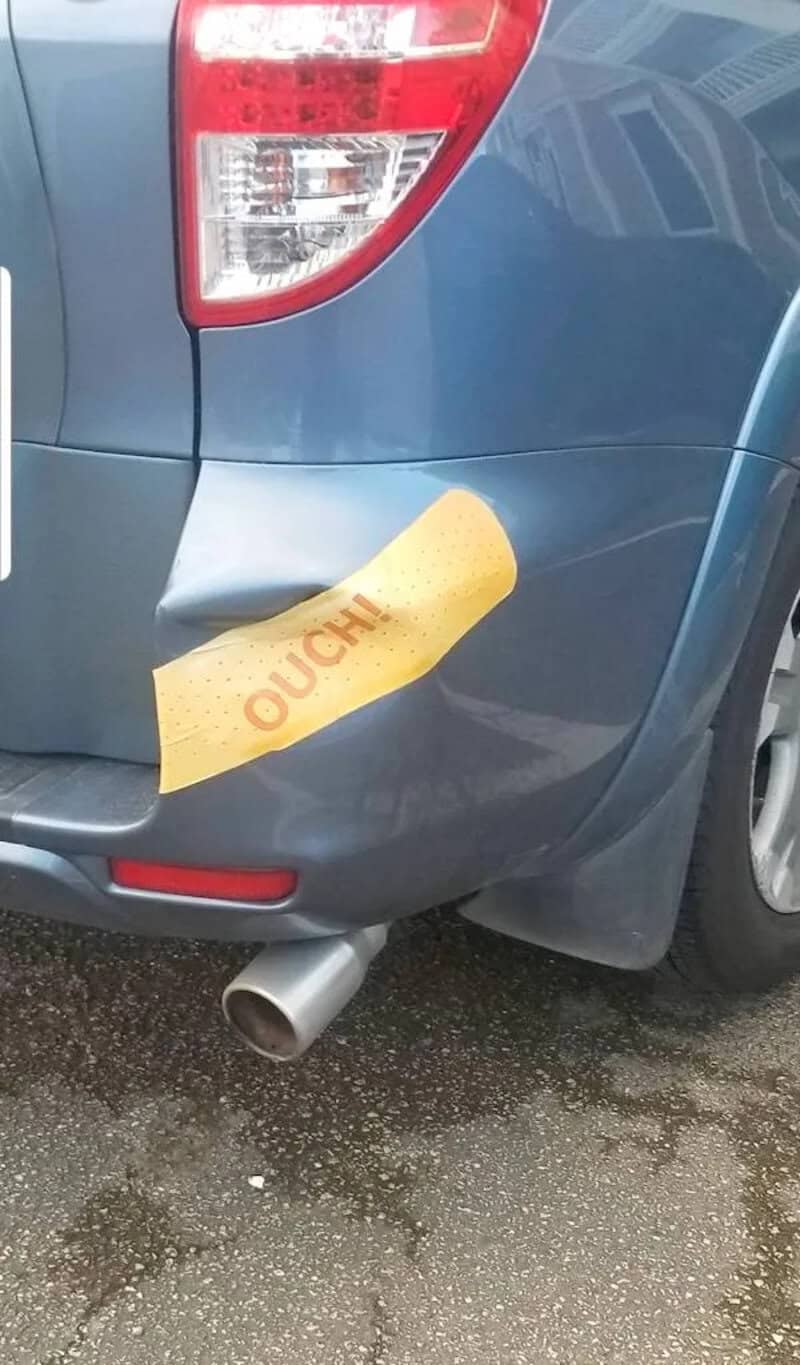 Car with a humorous "OUCH" sticker on the rear bumper after minor collision.