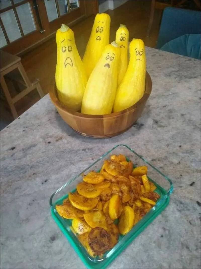 Yellow squash with hand-drawn faces in a wooden bowl, alongside a dish of cooked plantains on a kitc.
