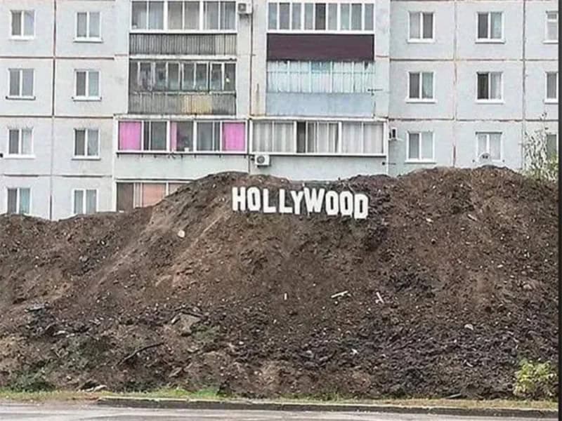 Humorous dirt mound with "Hollywood" sign parody in front of apartment building.
