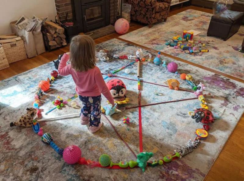 Child playing with a large circle of toys in a cozy living room.