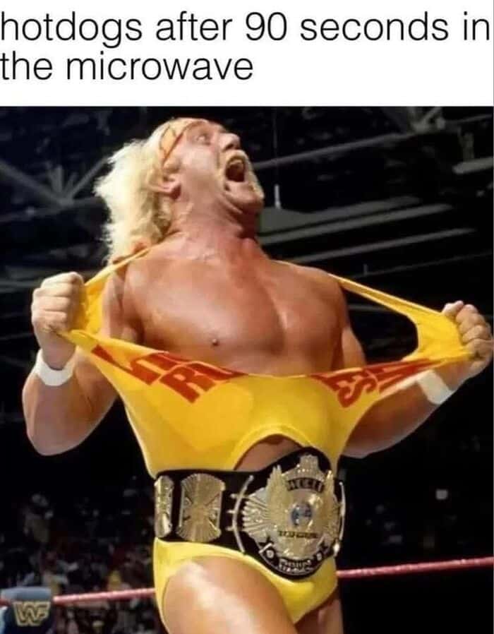 A woman wrestler pulling her yellow shirt with "R" visible, wearing a championship belt, celebrating.