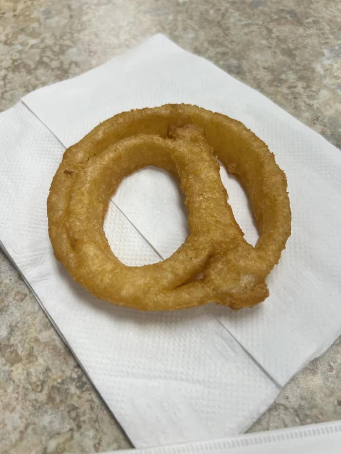 Golden fried onion rings on a paper towel on a gray surface.