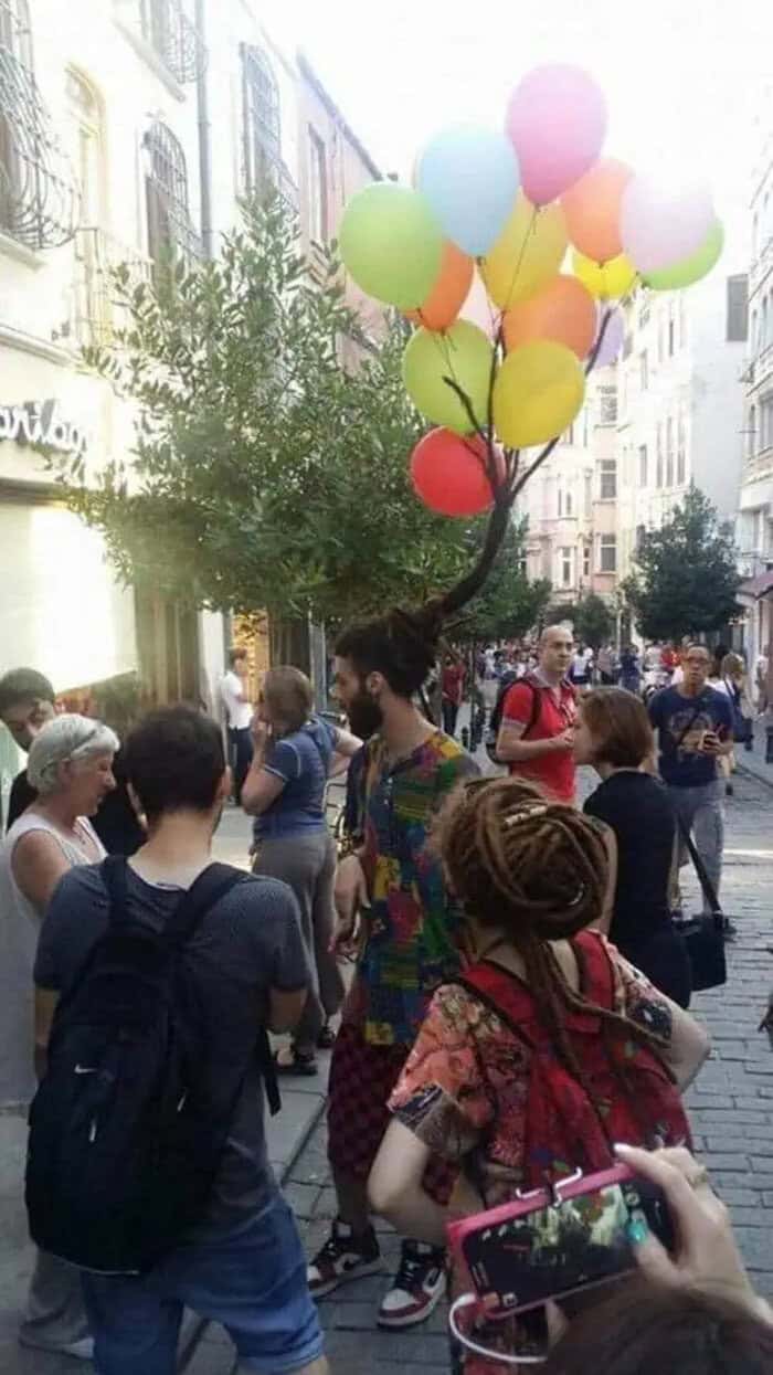 A colorful balloon tree performer entertaining a crowd on a city street.