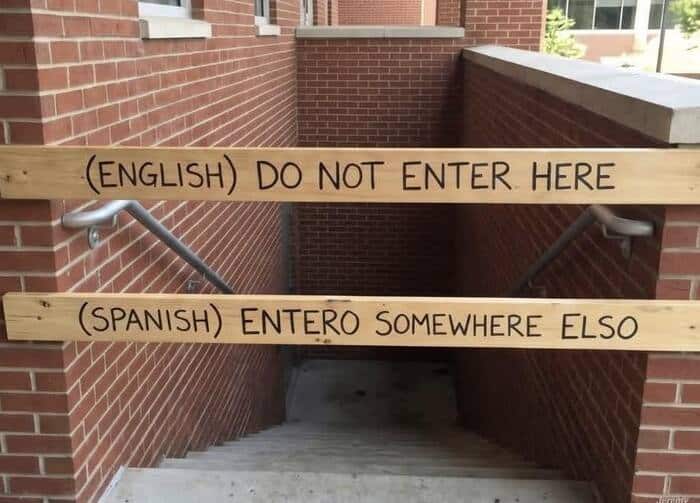 "Warning signs in English and Spanish on wooden planks over a stairway".