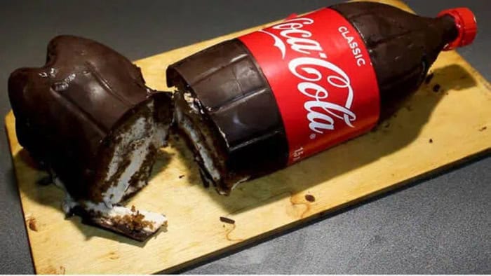 Coca-Cola bottle-shaped cake with a slice cut out on a wooden board.