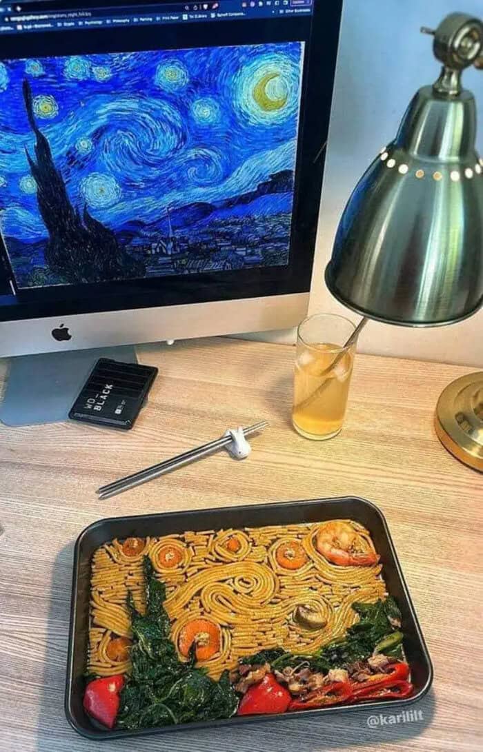 Van Gogh Starry Night inspired artwork on computer screen with pasta dish on desk.