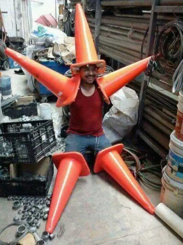A man wearing a red tank top with orange traffic cones attached to his body, forming a star shape.