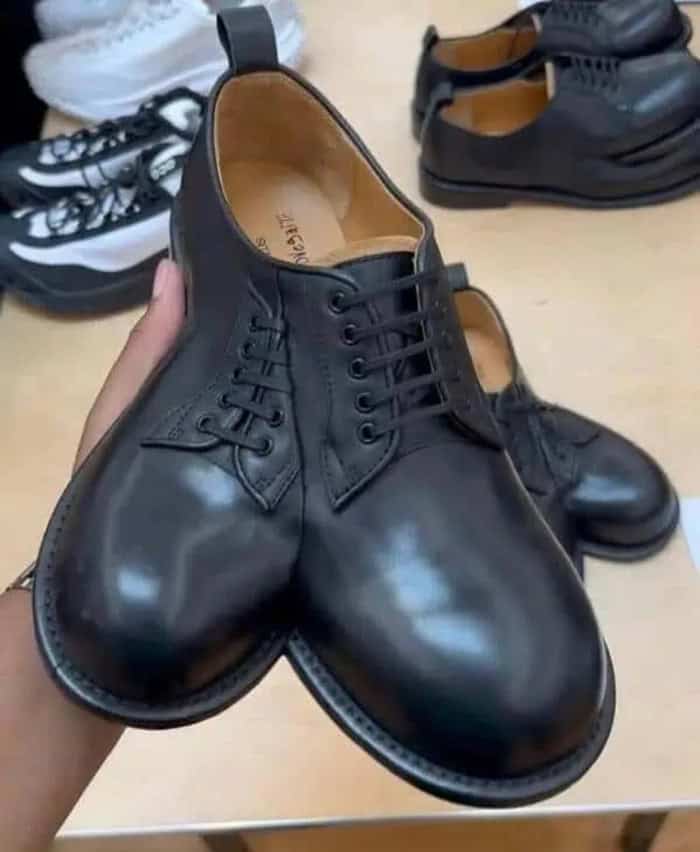 Black leather dress shoes with rounded toes and laces, displayed on a wooden surface.