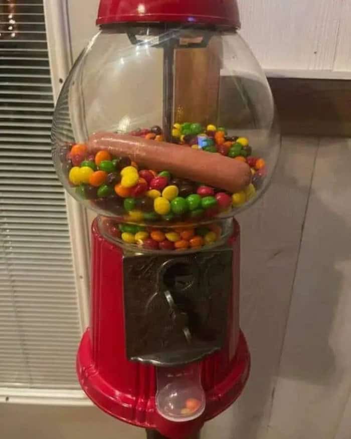 Gumball machine with a sausage and colorful candies inside.