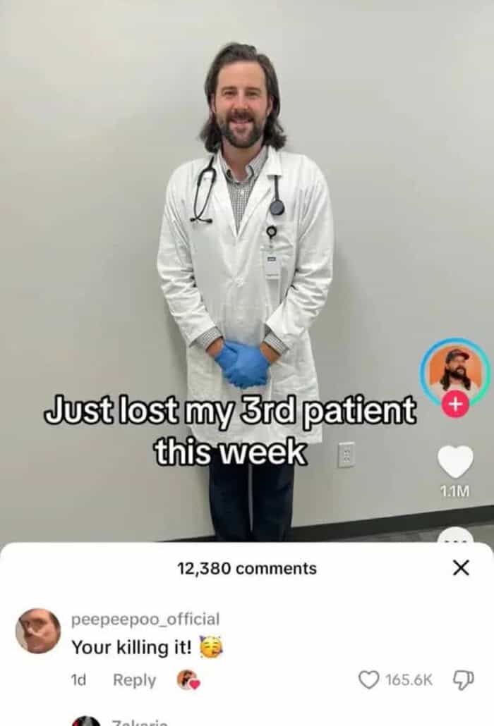 Doctor smiling in white coat with stethoscope, standing against plain wall.