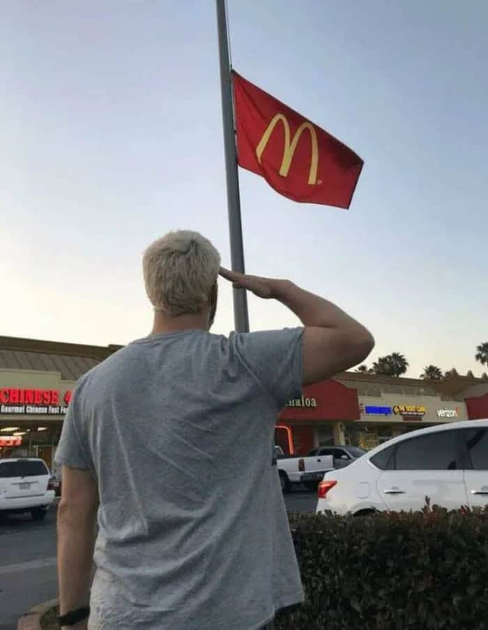 "Saluting the McDonald's flag outside a restaurant with cars parked nearby.".