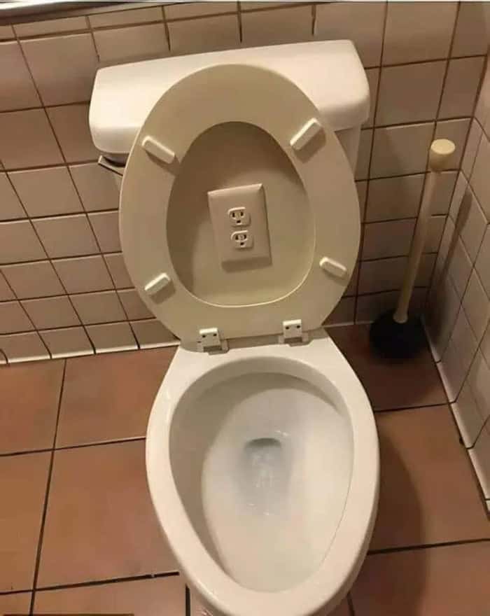 Toilet with electrical outlet inside the bowl, in a tiled bathroom.