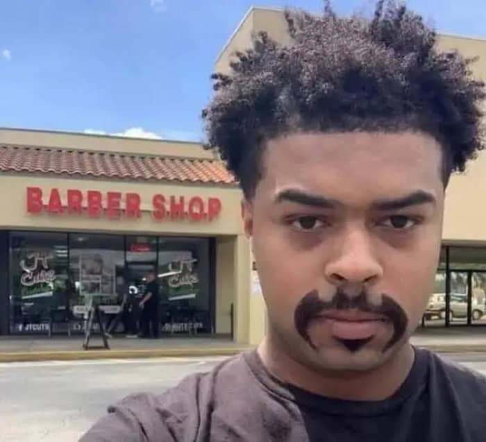 Man with a painted mustache and beard outside barber shop.