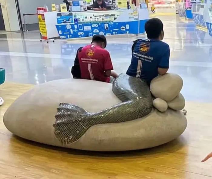 Two people sitting on a large stone with a snake sculpture in a store.