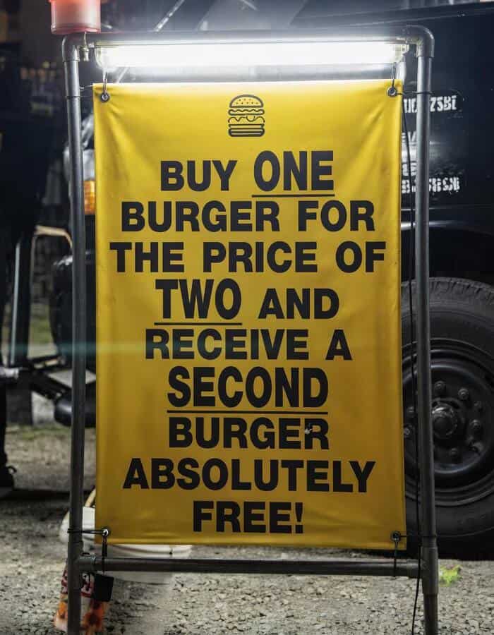Buy one burger for the price of two, get a second burger free sign at a food stand.