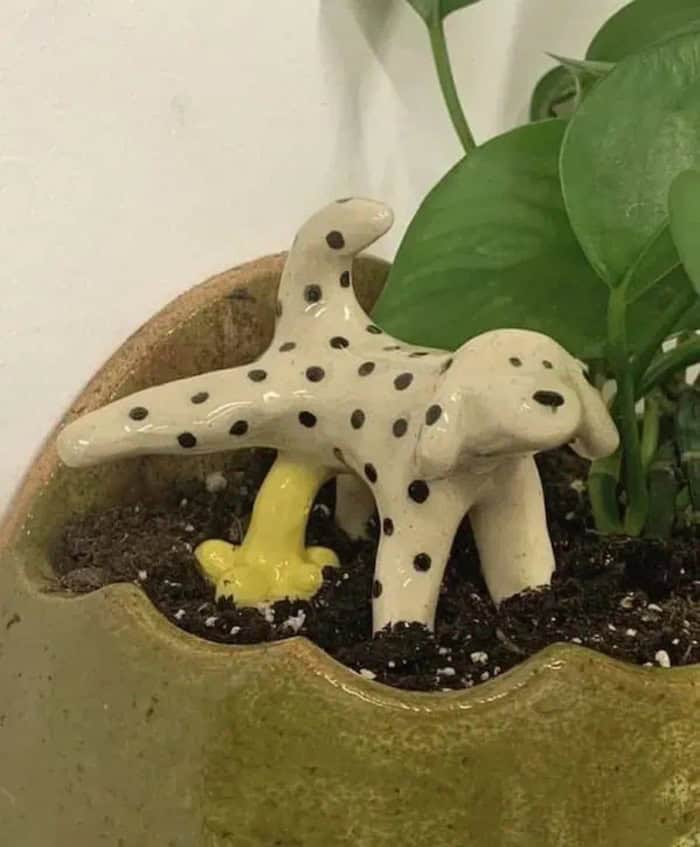 Cute ceramic dog and dinosaur figurines in a plant pot with soil and green leaves.