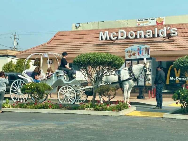 Horse-drawn carriage parked at McDonald's drive-thru with customers and staff.