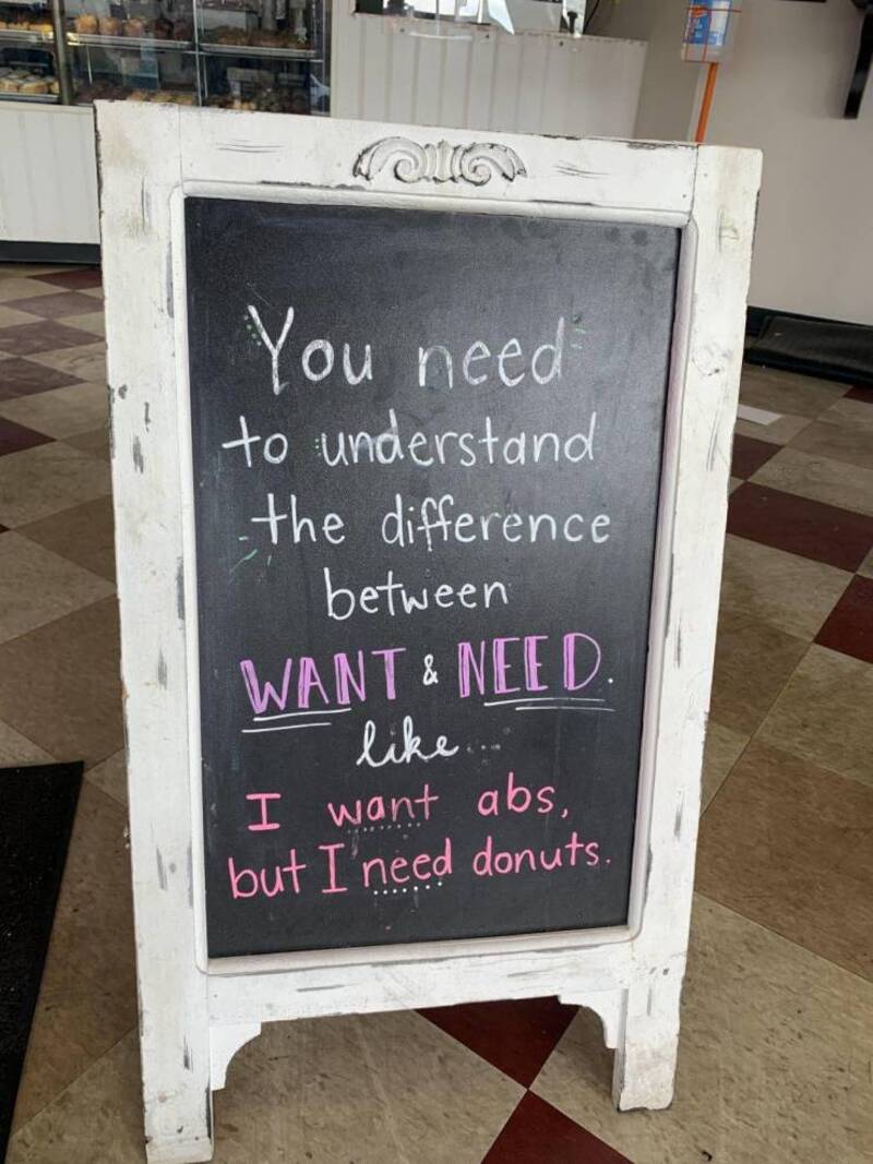 Chalkboard sign with humorous message about wants and needs, highlighting the importance of donuts o.