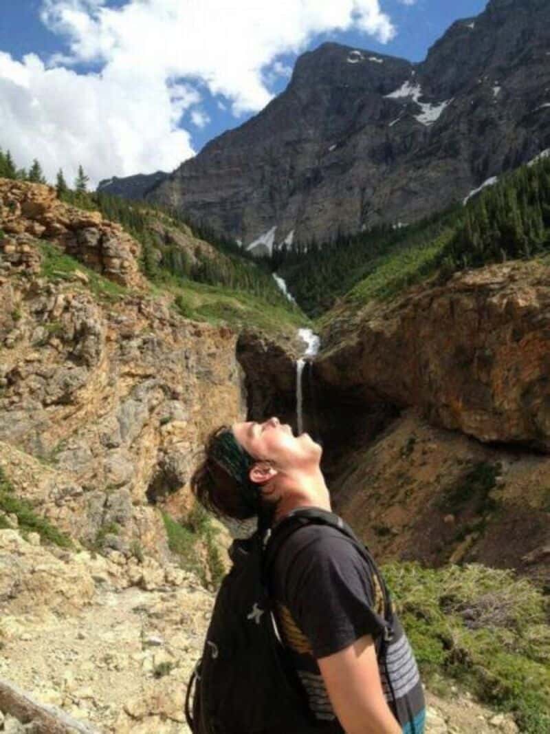 Waterfall flowing from mountain into valley with lush greenery.