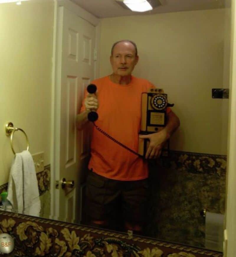 Vintage rotary phone, man in orange shirt, bathroom mirror selfie.