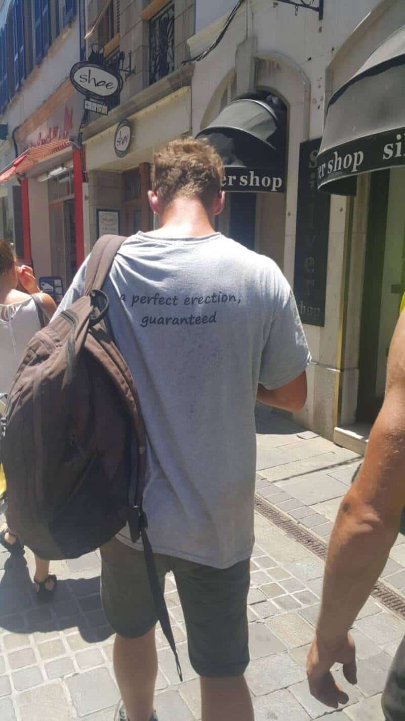 Man with humorous T-shirt reading "Perfect erection, guaranteed" in an urban setting.