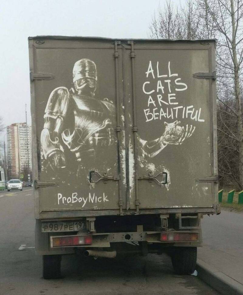 Graffiti of a robot holding a cat with the message "All cats are beautiful" on a truck door.